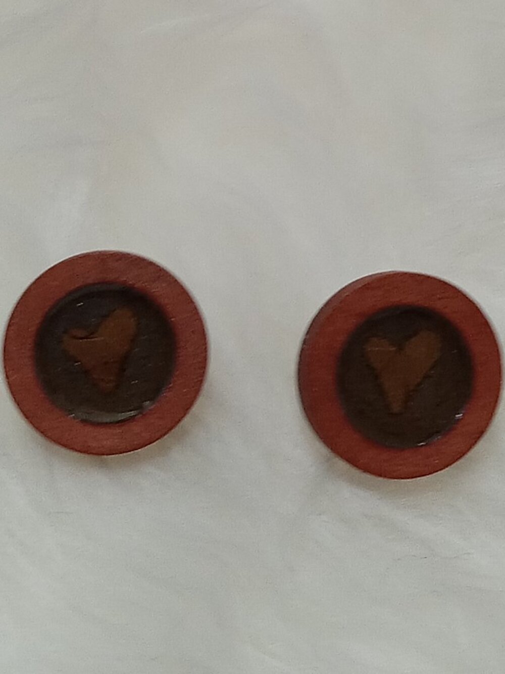 Handmade earrings on a wooden base with a piece of punched-out tree leaf